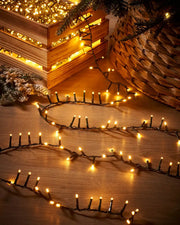 Warm white string lights clustered together on s wooden floor next to a Christmas tree and box 