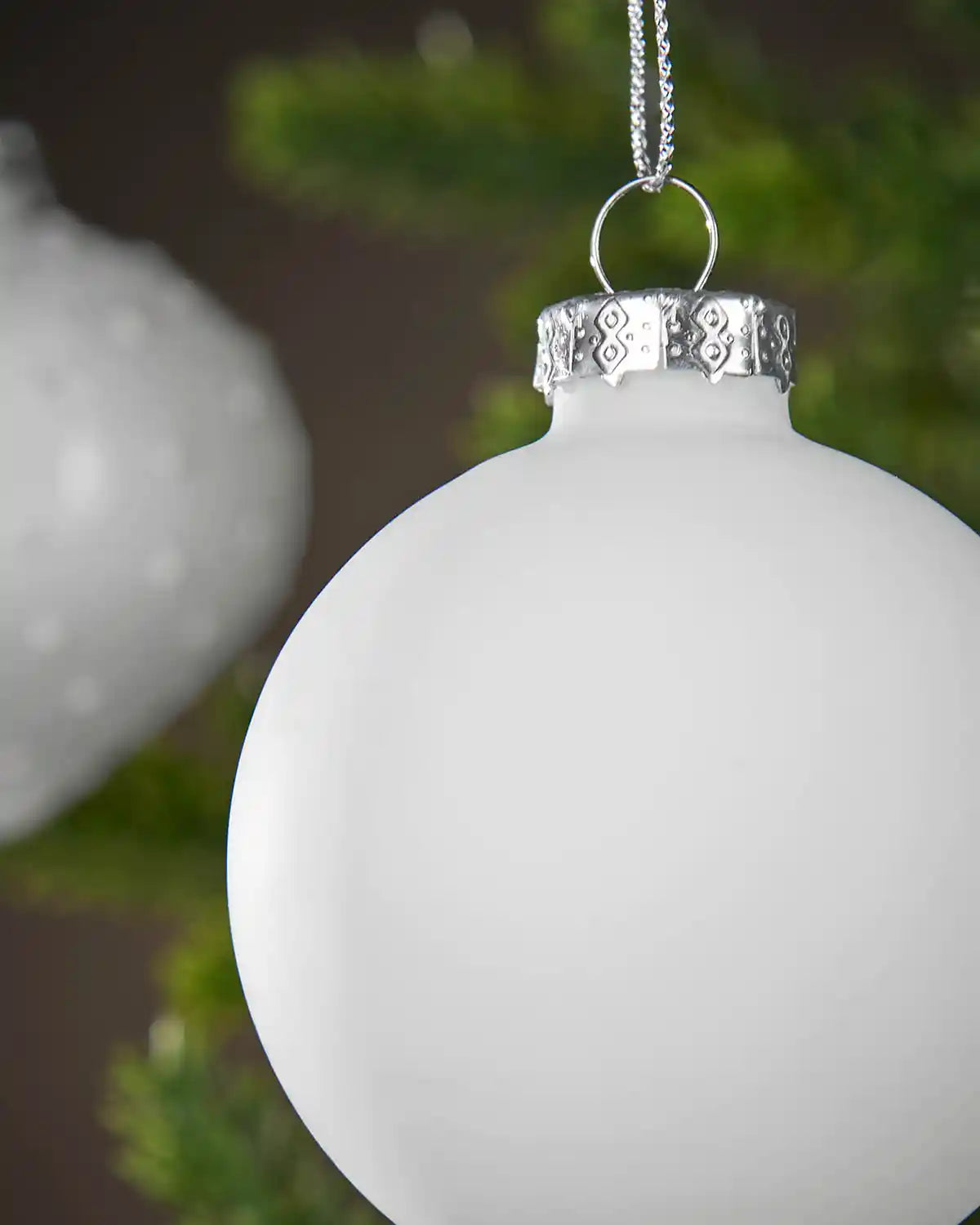 White Christmas ornament with silver cap on a blurred green background