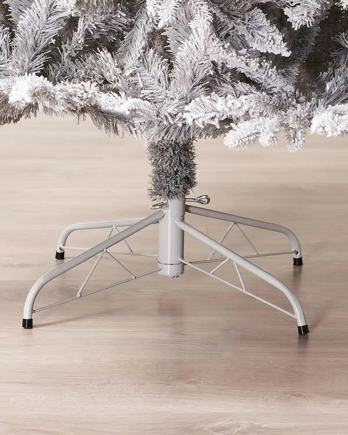 White Christmas tree stand with a Snow flocked Christmas tree on a wooden floor.