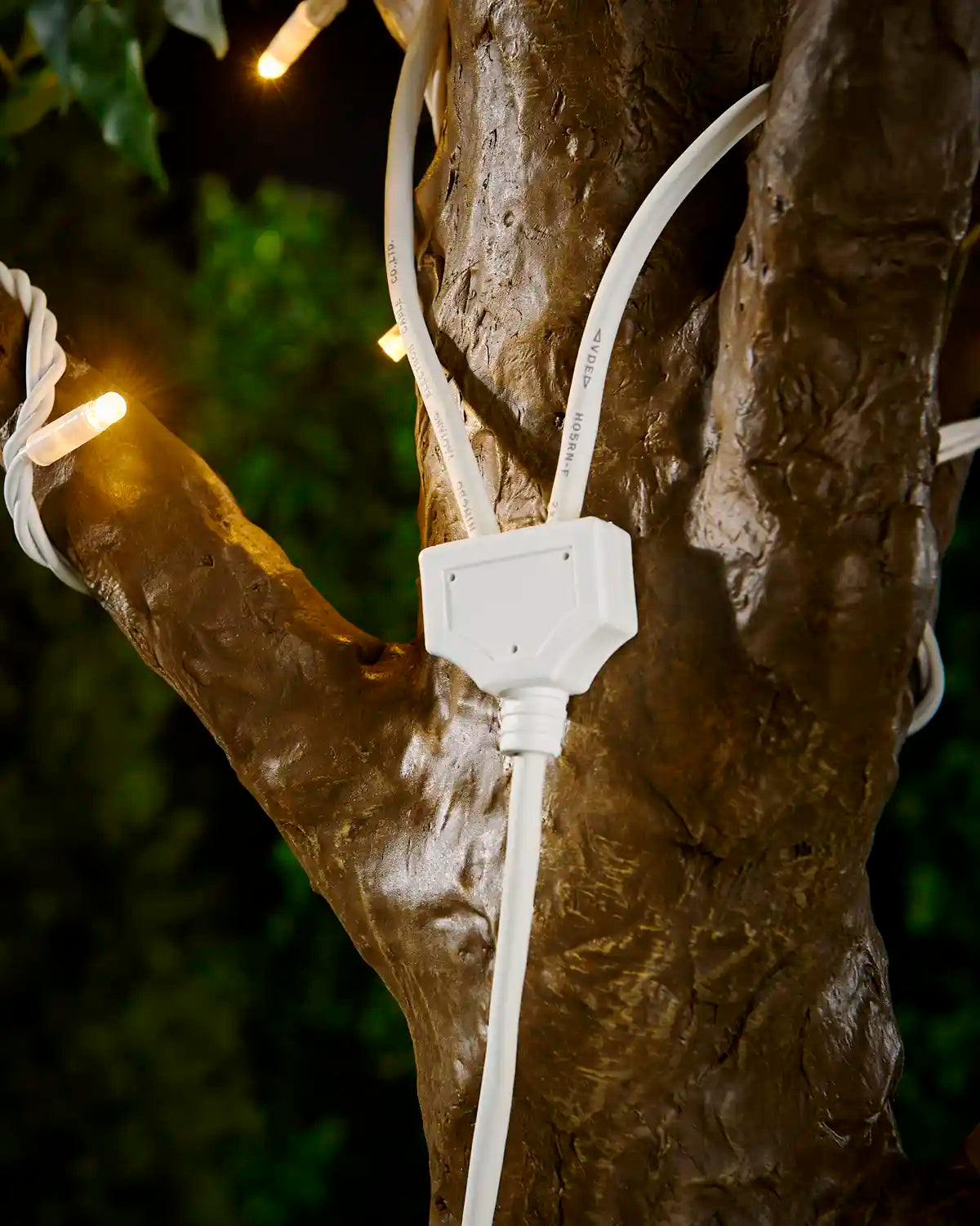 White Y shaped connector cable attached to tree with warm white LED string light with a blurry garden background
