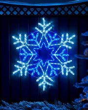 White and Blue LED lights in the shape of a Christmas snowflake on a garden fence with a snowy background