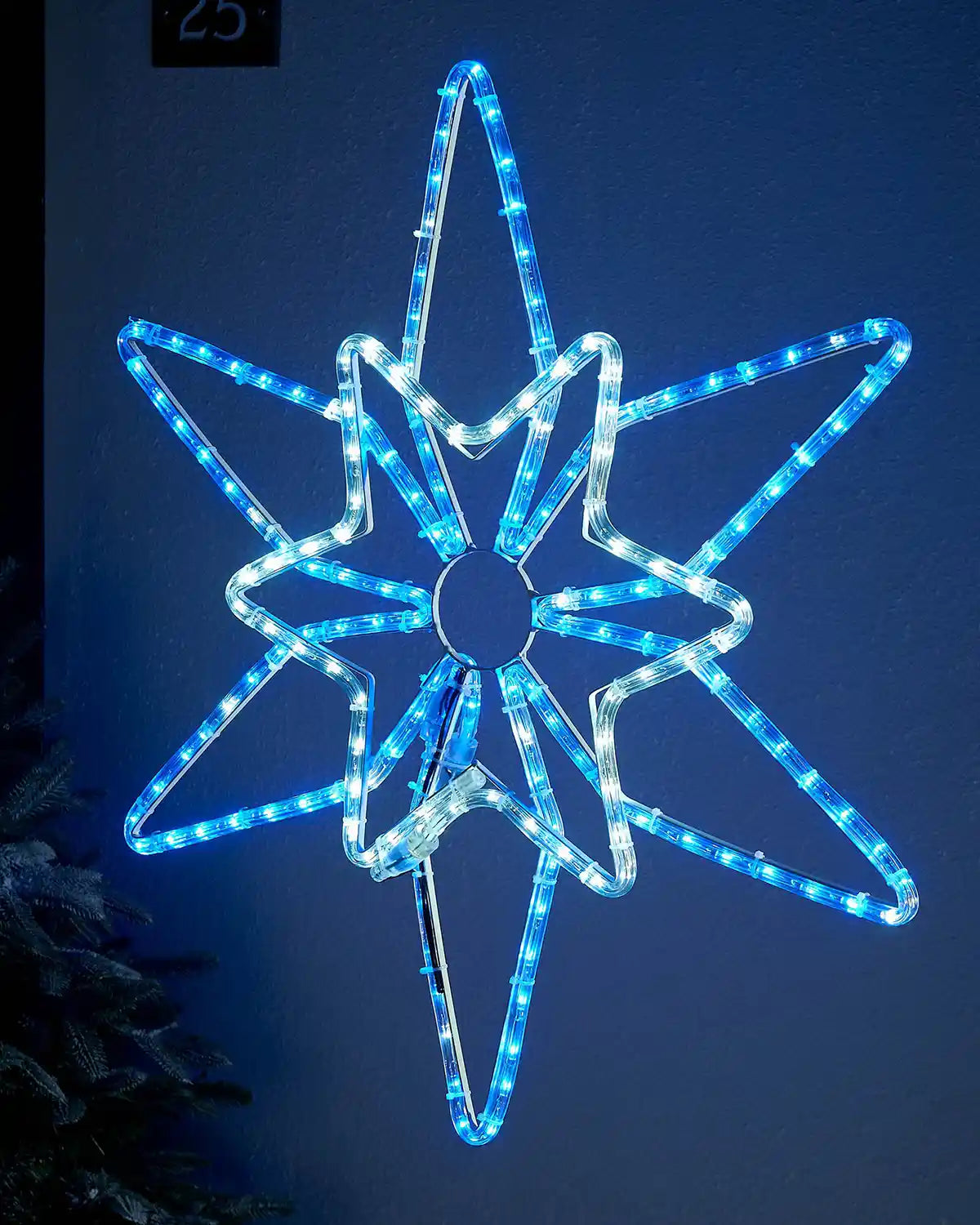 White and blue LED lights in the shape of the Northern star silhouette on a dark blue garden wall