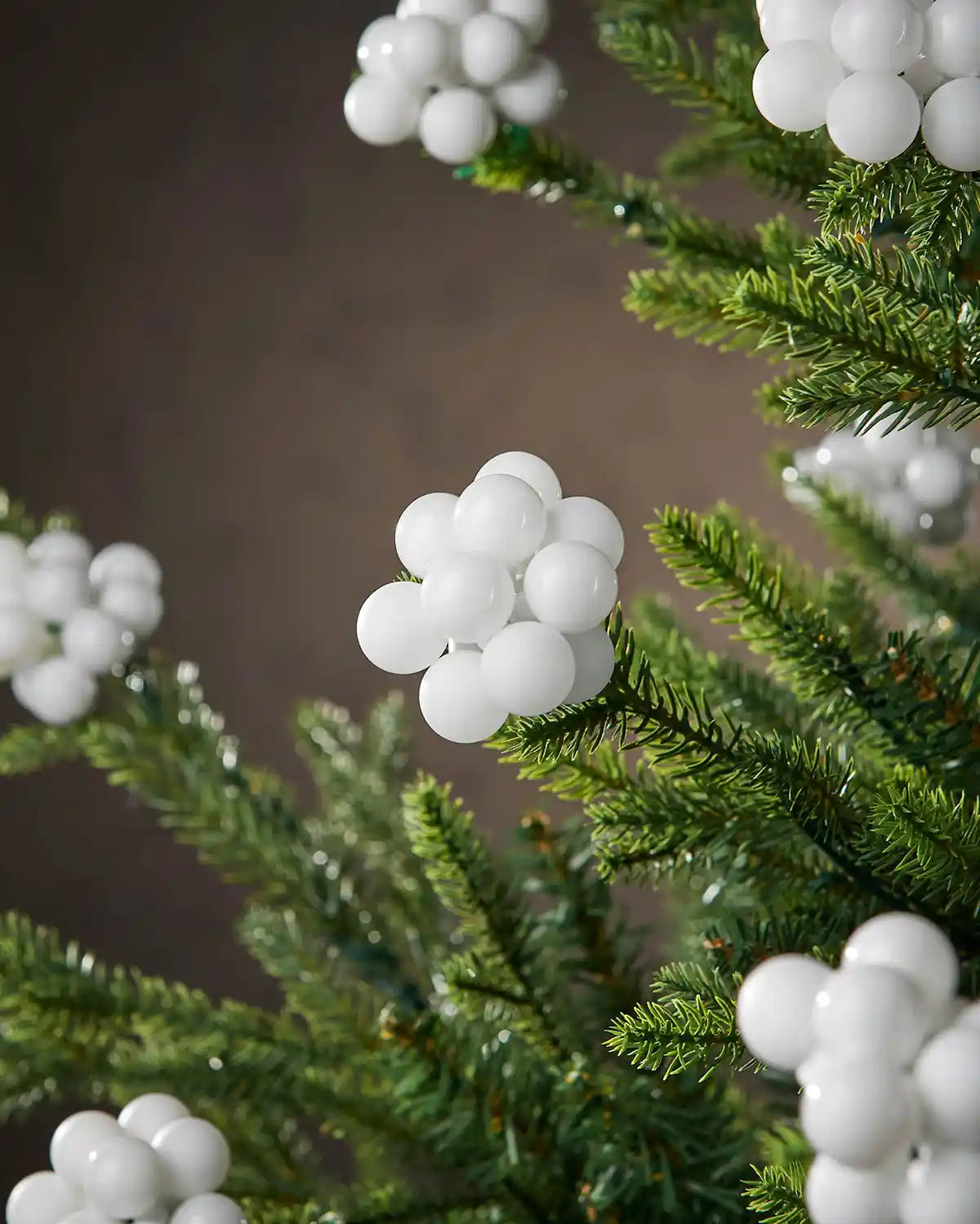 White bauble berry clusters on a Christmas tree branch against a brown background