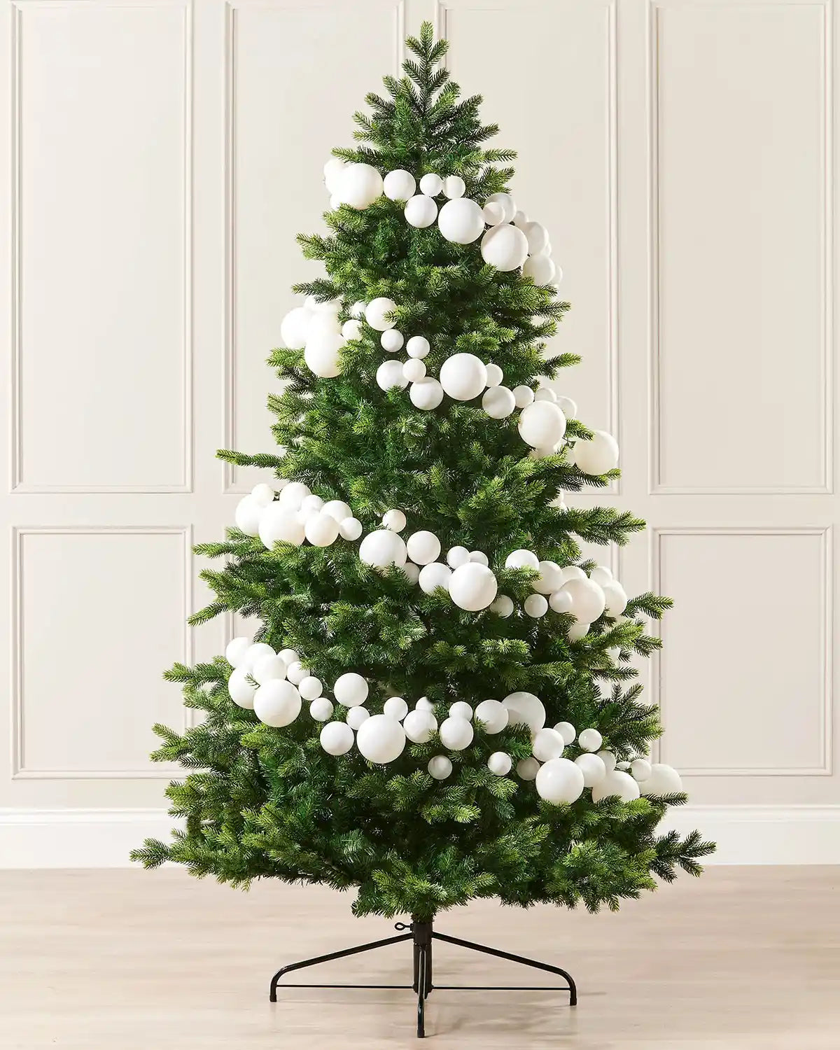 White bauble garland wrapped around a Christmas tree against a cream panel wall and a wooden floor 
