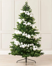 White bauble garland wrapped around a Christmas tree against a cream panel wall and a wooden floor 

