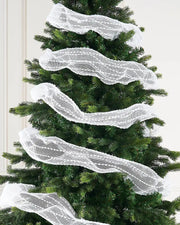 White decorative mesh ribbon with lace pattern wrapped around Christmas tree against cream wall