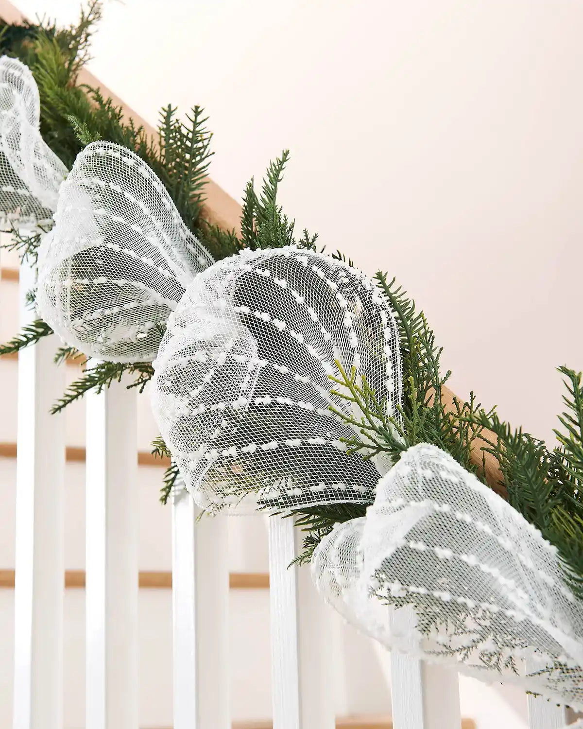 White lace pattern mesh ribbon wrapped around garland on a white staircase banister 