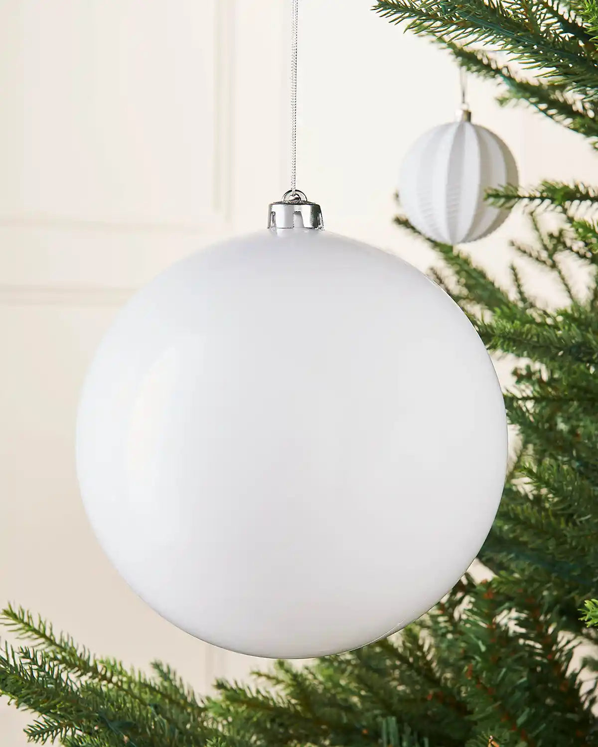 White oversized gloss bauble on a Christmas tree accompanied by a smaller white bauble