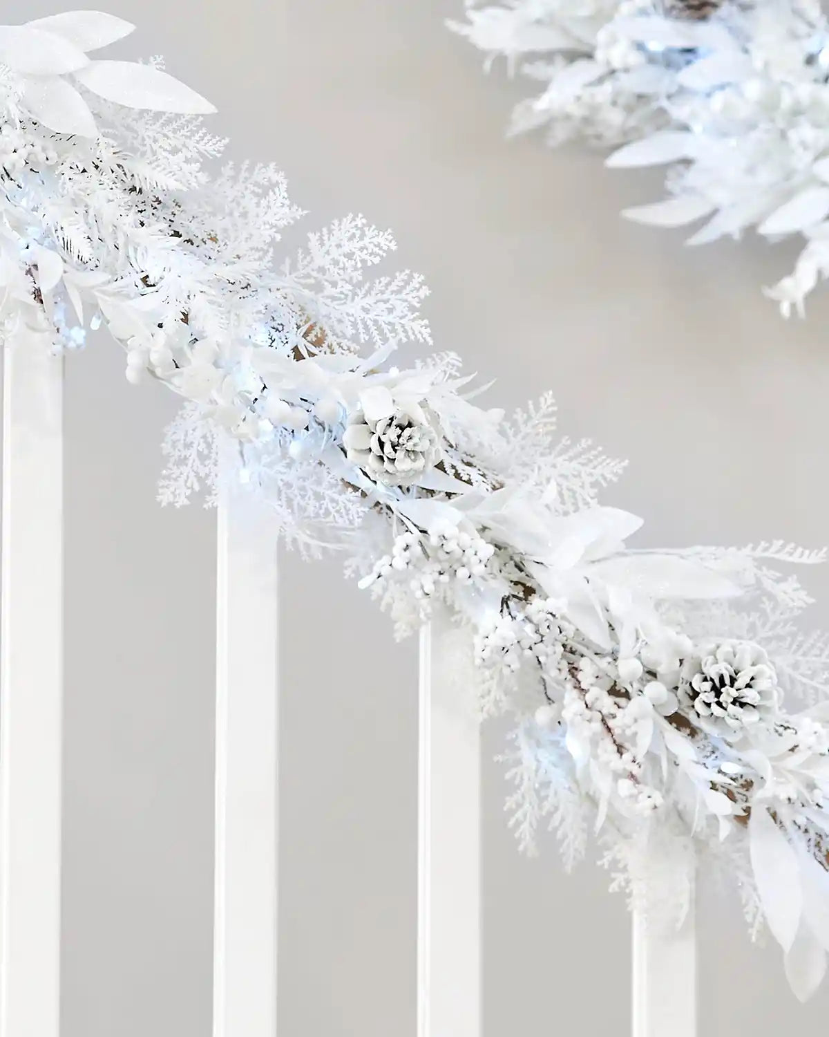 White snow flocked garland with berries and pinecones on a staircase banister against a cream wall