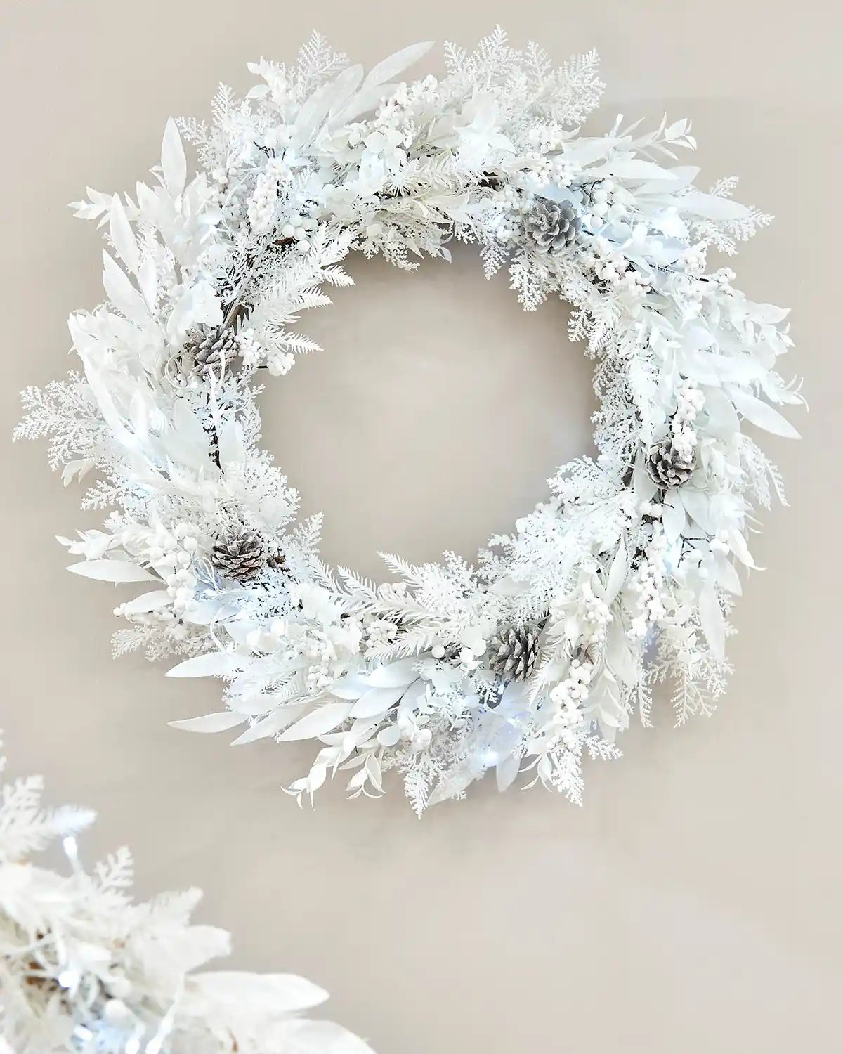 White snow flocked wreath with ice white lights and pinecones on a cream wall