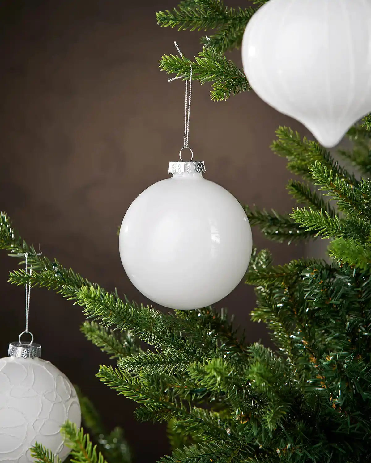 White spherical Christmas ornament hanging on a tree branch with a dark background