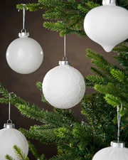 White textured Christmas ornaments on a green tree against a brown background