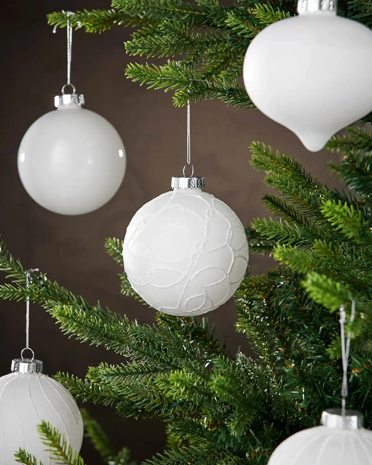 White textured Christmas ornaments on a green tree against a brown background
