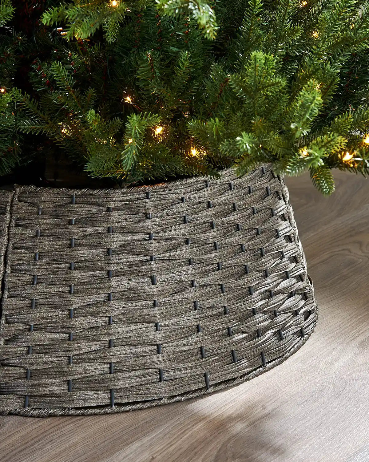 Woven grey tree 
collar under a decorated Christmas tree on a wooden floor.
