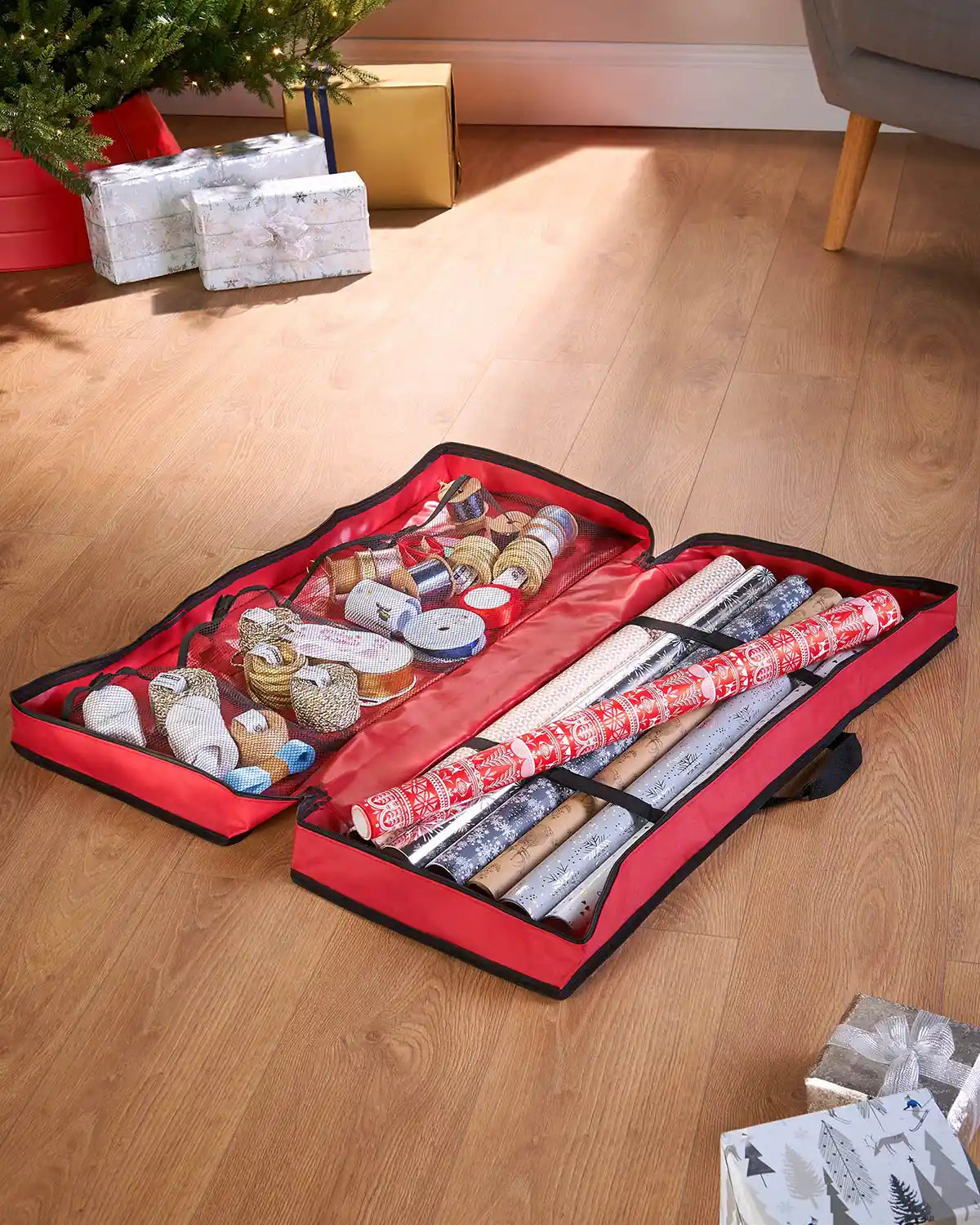 Long shot of open Wrapping Paper Storage Bag open with wrapping paper ribbon and a mesh lining with a Christmas tree background and wooden floor