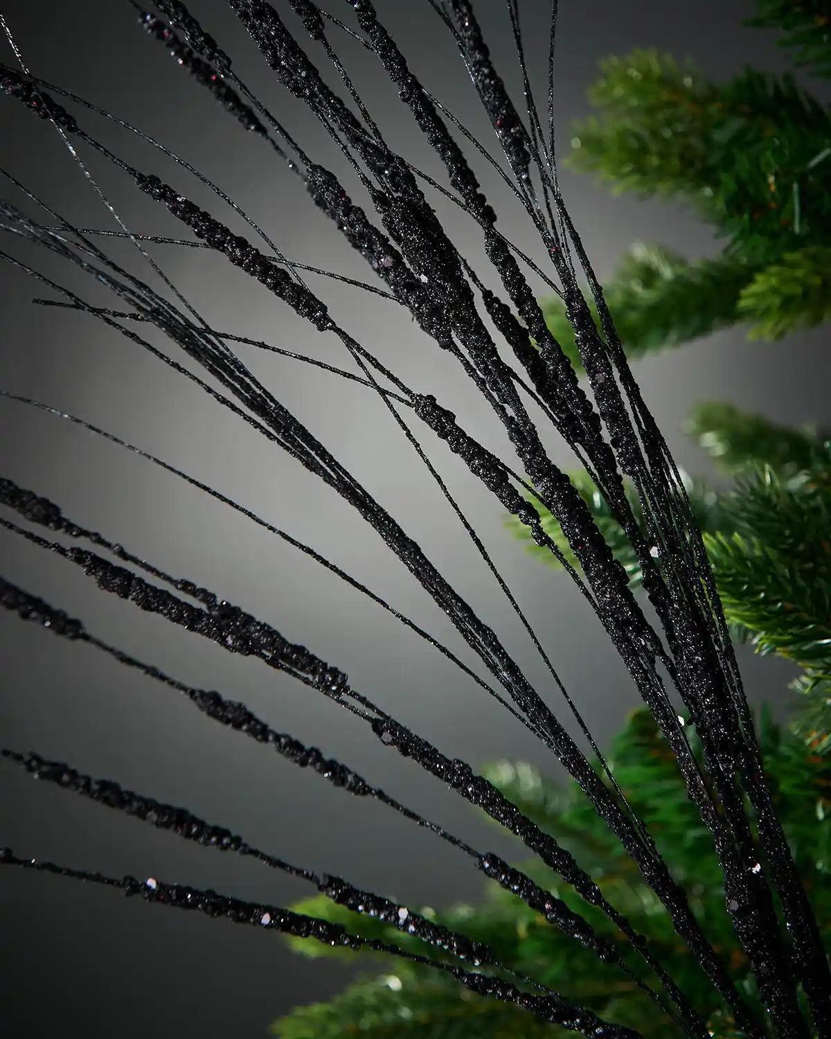 Zoomed-in image of 100cm black glitter tree spray attached to Christmas tree in front of grey background