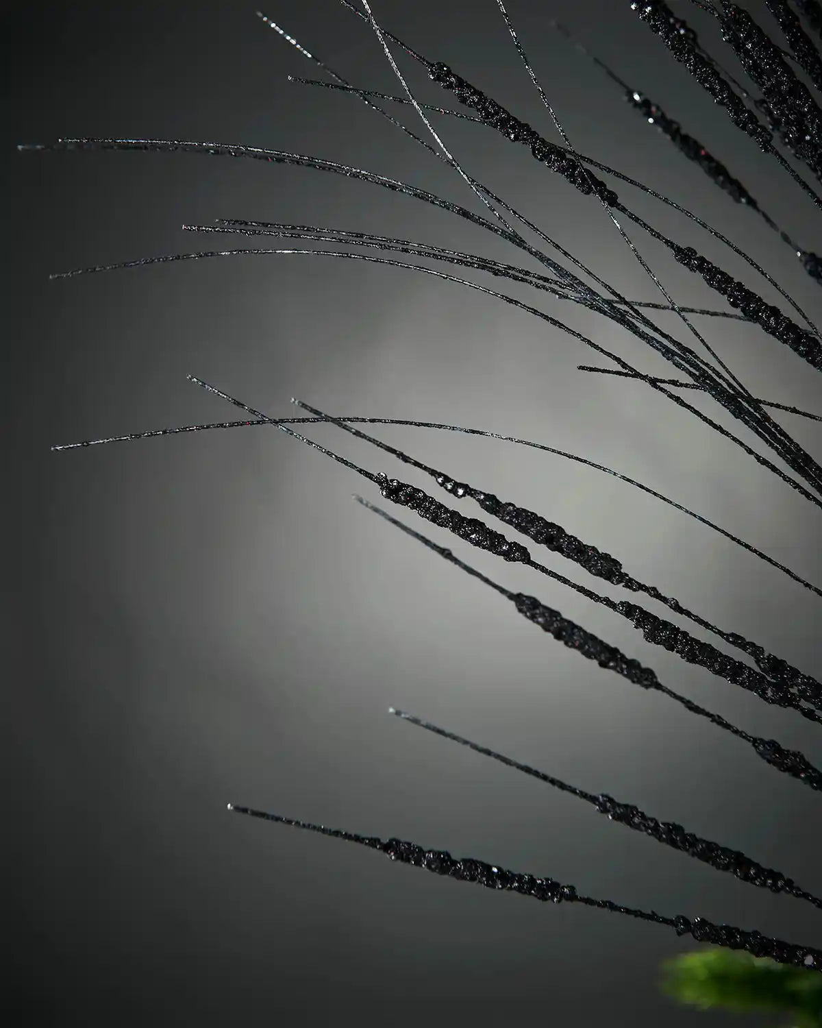 Zoomed-in image of 100cm black glitter tree spray in front of grey background highlighting sequin sparkle