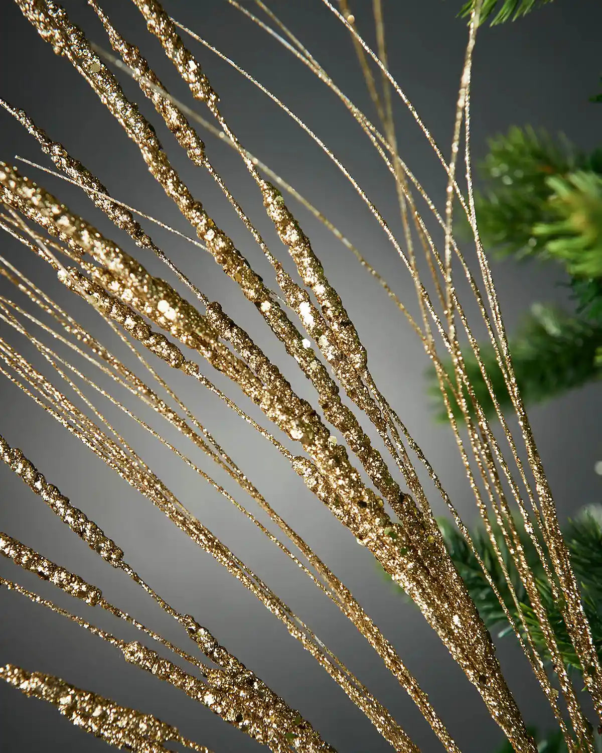 Zoomed-in image of 100cm gold glitter wispy spray in front of grey background highlighting sparkle