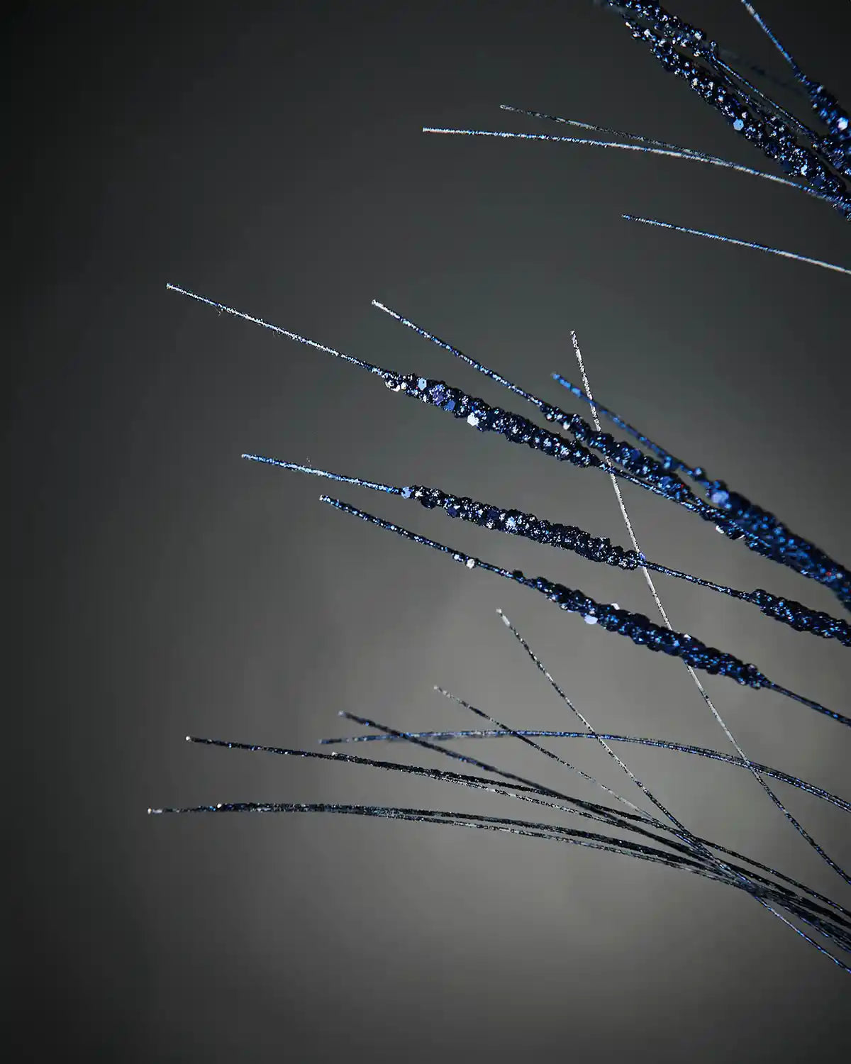 Zoom-in of 100cm navy blue glitter wispy tree spray highlighting sequin branches in front of grey wall background