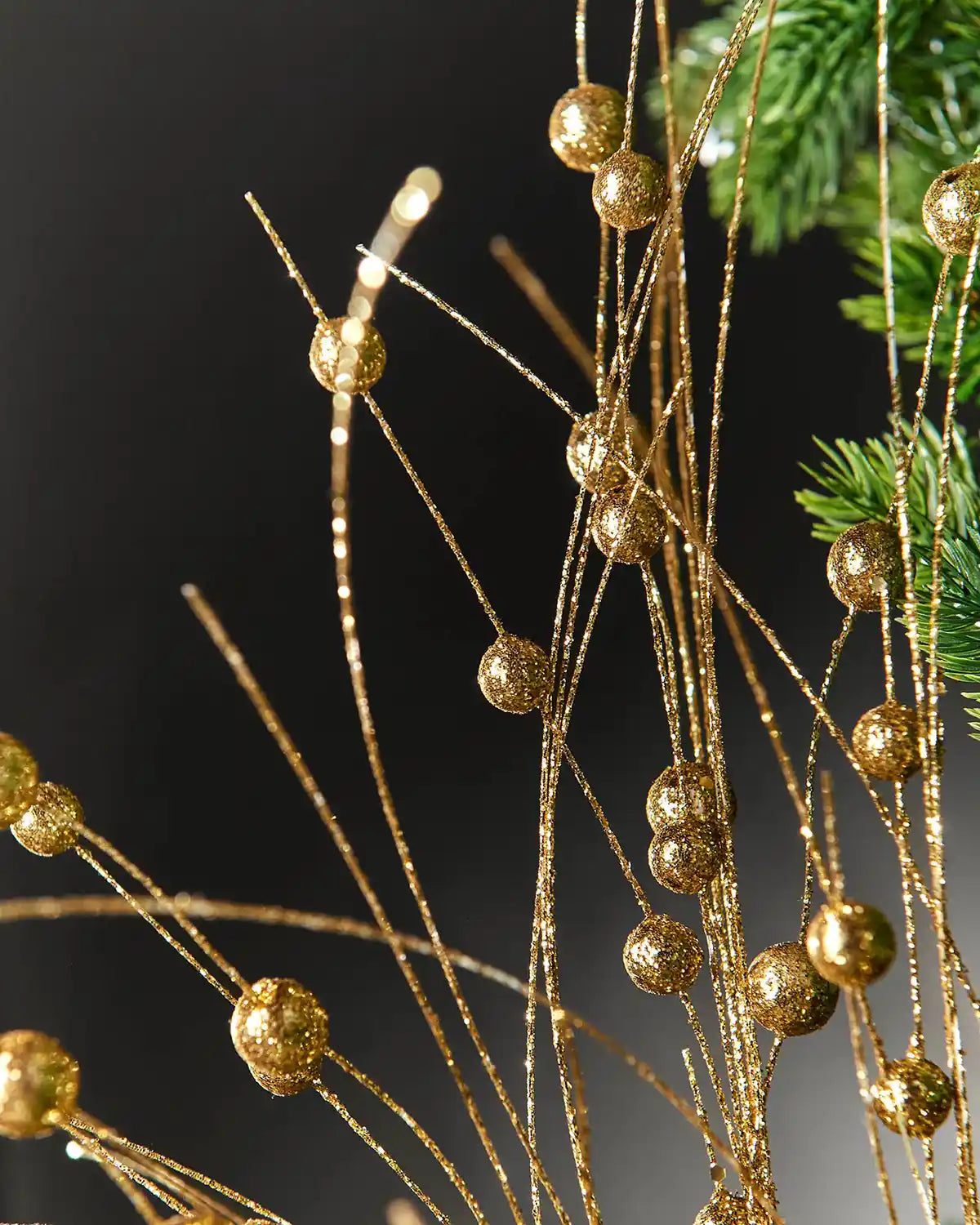 Zoomed-in image of the gold berry glitter spray attached to a Christmas tree in front of grey wall background highlighting glitter effect