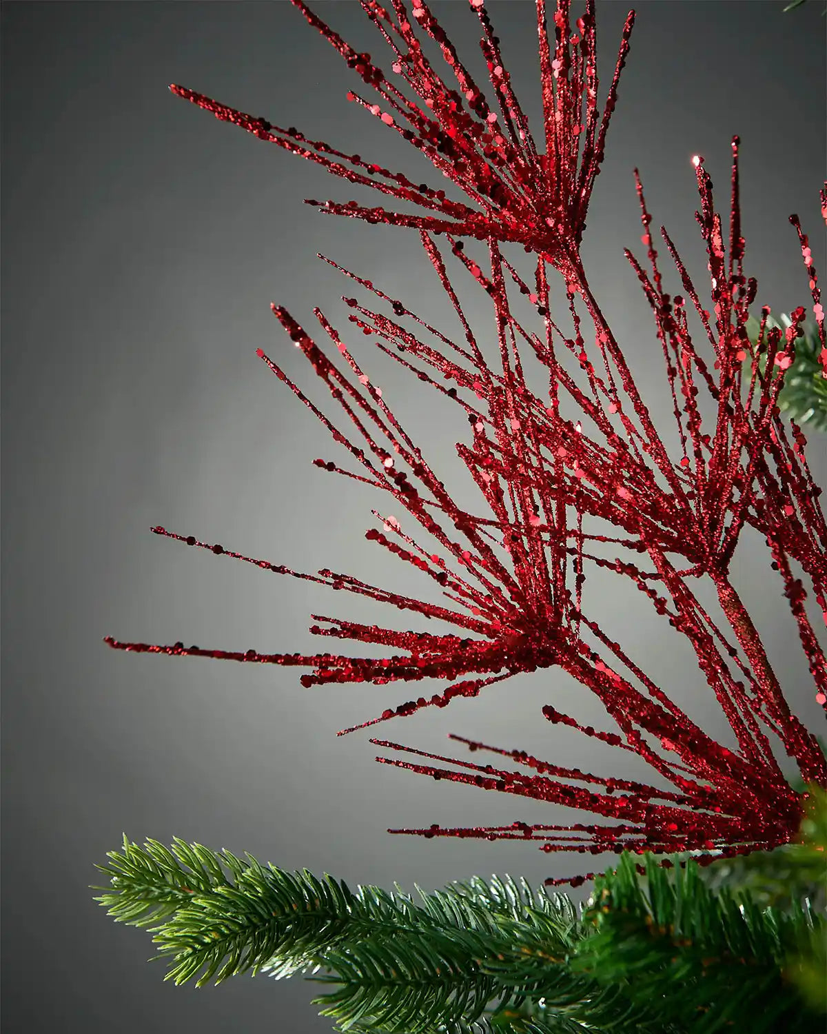 A zoom-in on red glitter bauble spray attached to Christmas tree in front of grey background