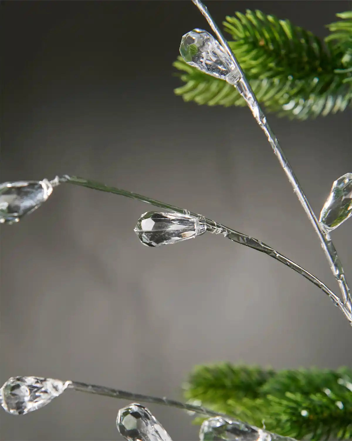 Zoomed-in image of silver crystal teardrop spray hanging on Christmas tree in front of grey wall background to highlight crystals
