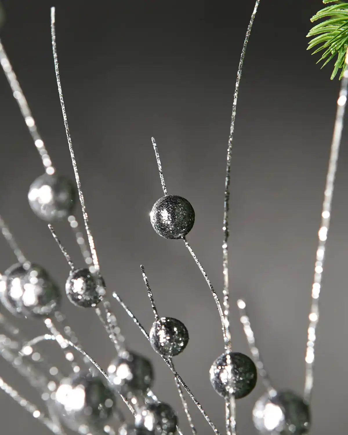 Zoomed-in image of silver glitter berries spray in front of grey wall background highlighting shimmer effect