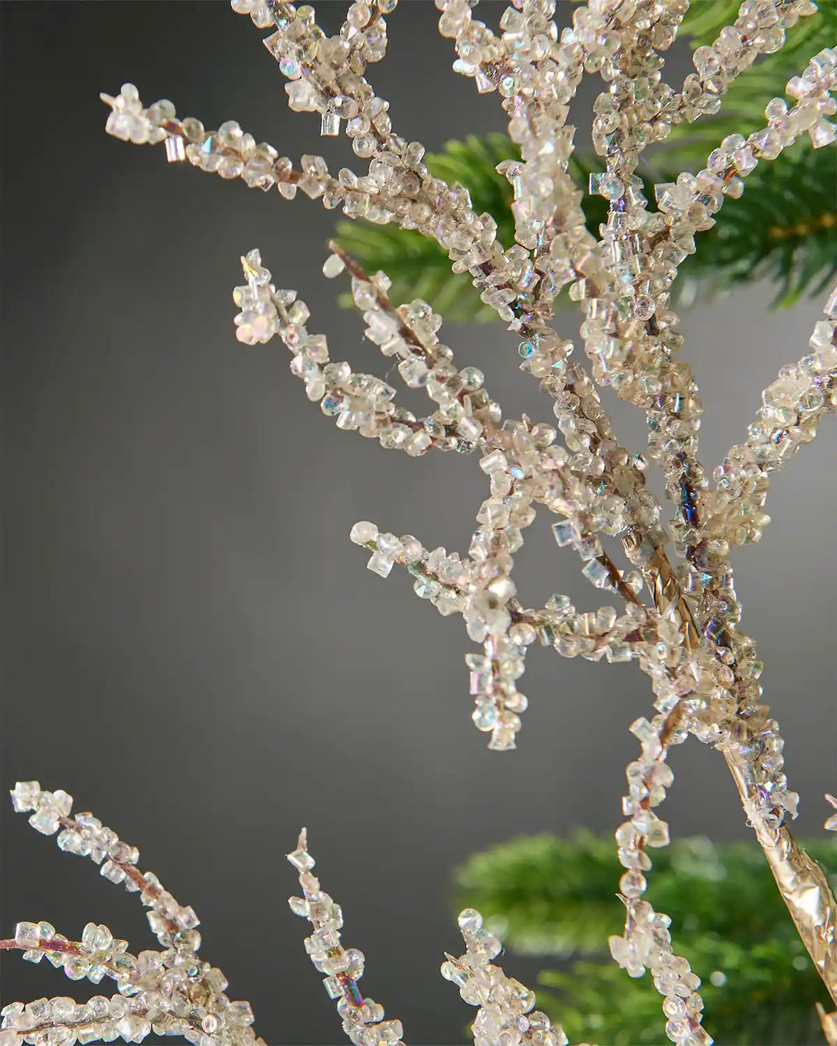Zoomed-in gold beaded crystal spray attached to Christmas tree in front of  grey wall background highlighting shine of beads