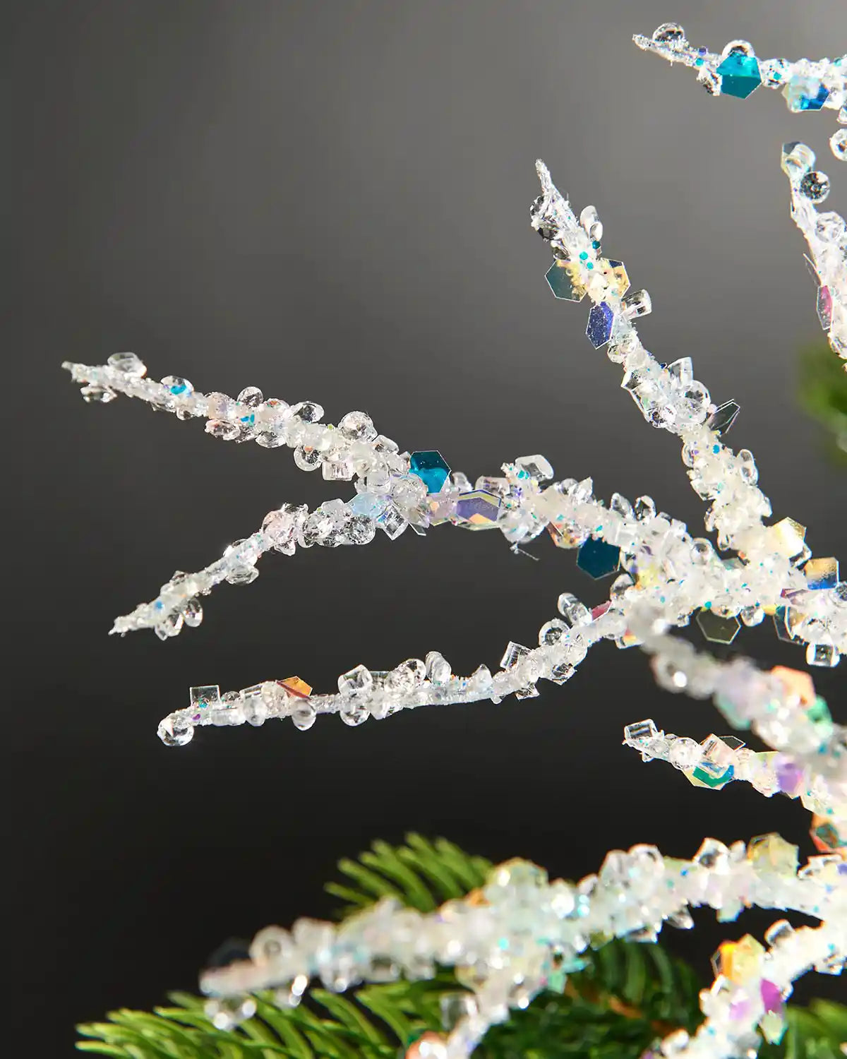 Zoomed-in image of white beaded crystal spray on tree in front of grey wall background highlighting iridescent sequins
