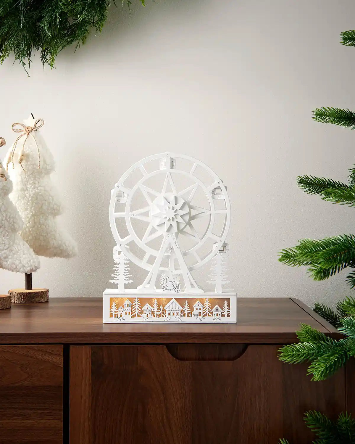 Zoomed out alternative full image of pre lit white animated ferris wheel with warm white lighting on dark surface in front of white wall