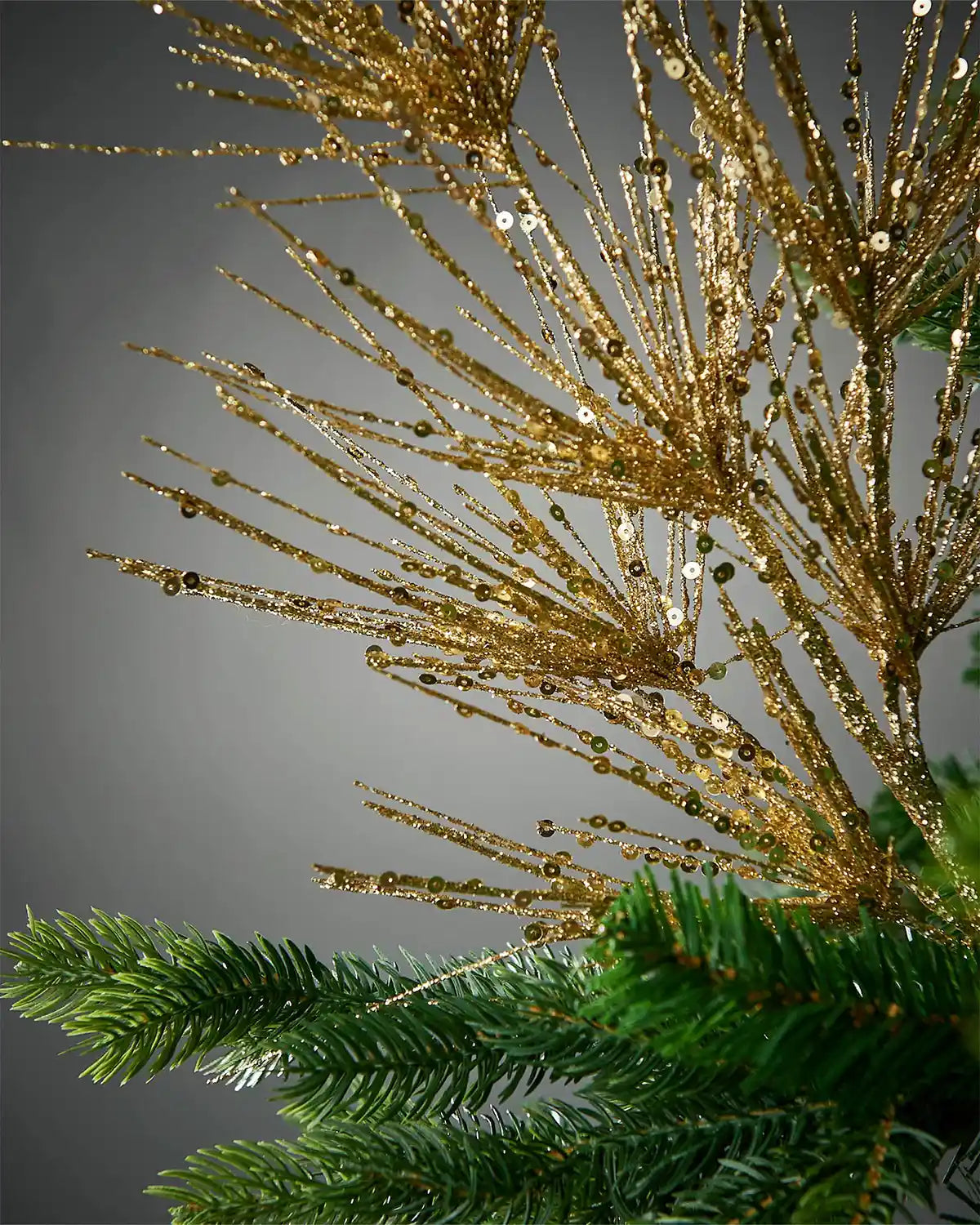 Zoomed-in image of gold glitter firework spray attached to Christmas tree in front of grey background
