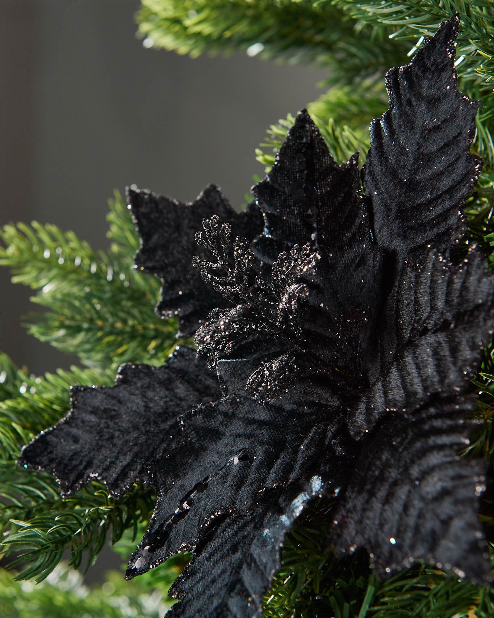 Close-up of a 25 cm artificial black poinsettia flower showing layered petals and a glittered centre.