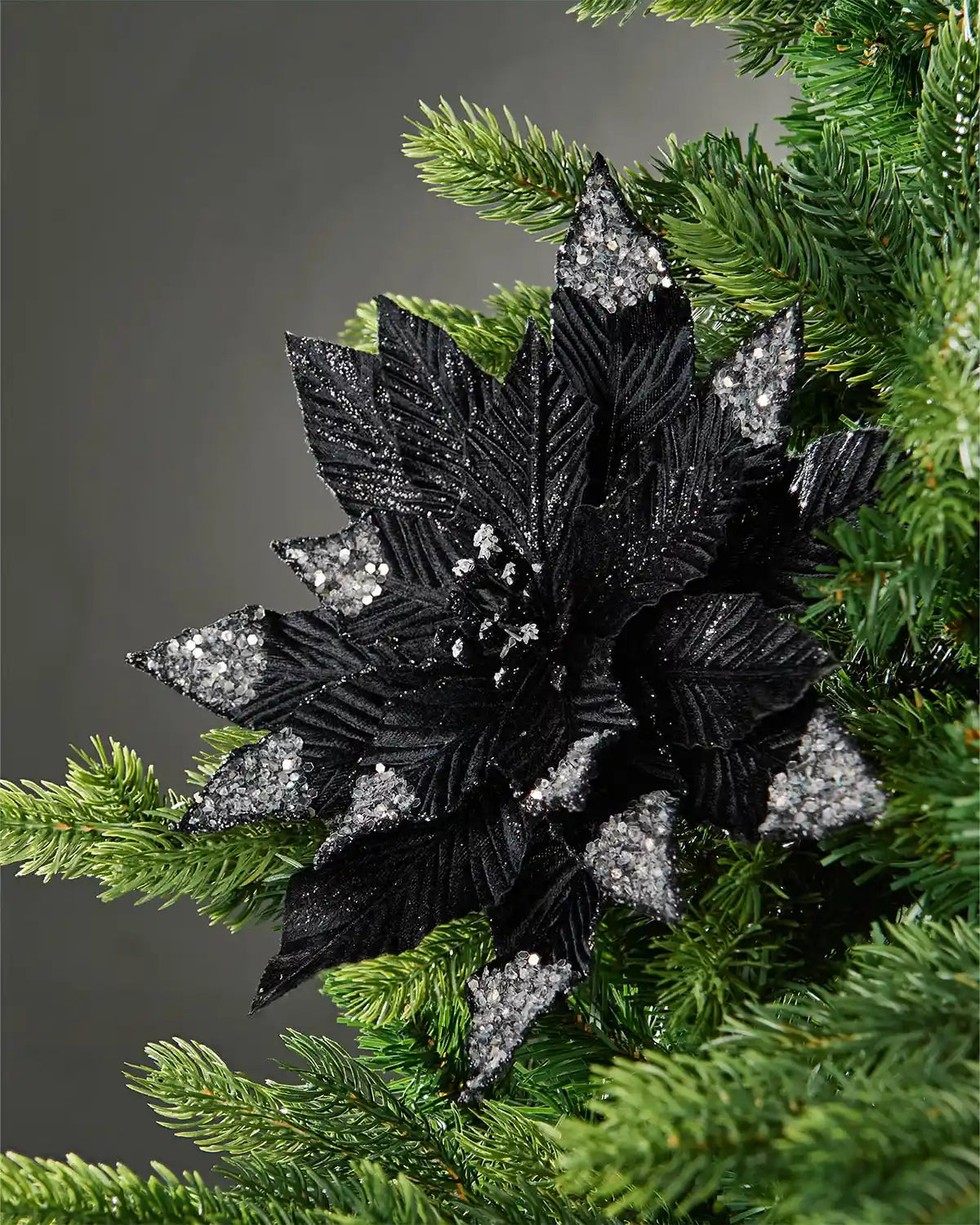 28 cm artificial black poinsettia flower displayed in a Christmas tree, with silver glitter-tipped petals and a jewelled centre.