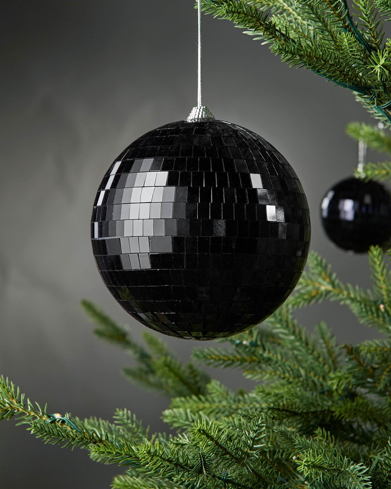 Black 15cm oversized disco ball bauble hanging on a Christmas tree.