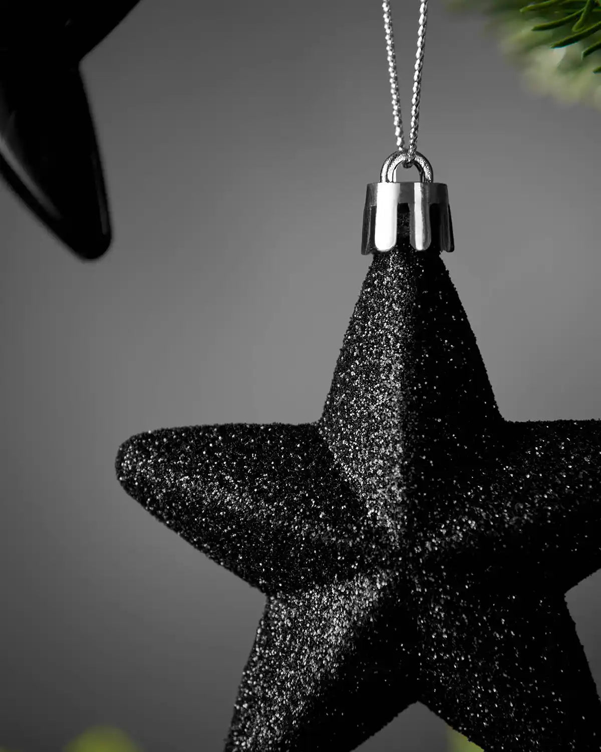 Close-up of a black 7cm glitter hanging star with silver cap and string.