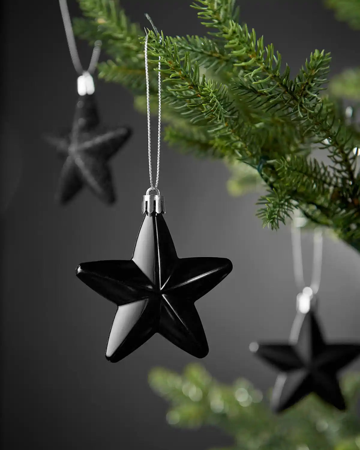 Close-up of a shiny black 7cm hanging star with silver string on a Christmas tree.