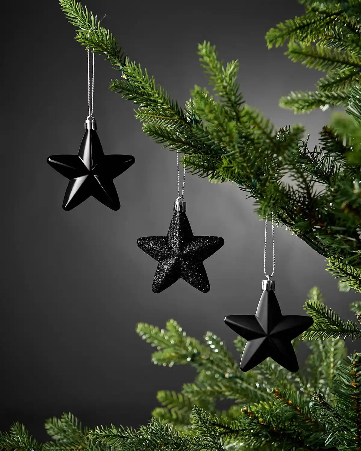 Black 7cm hanging star decorations in shiny, glitter and matte finishes displayed on a Christmas tree.