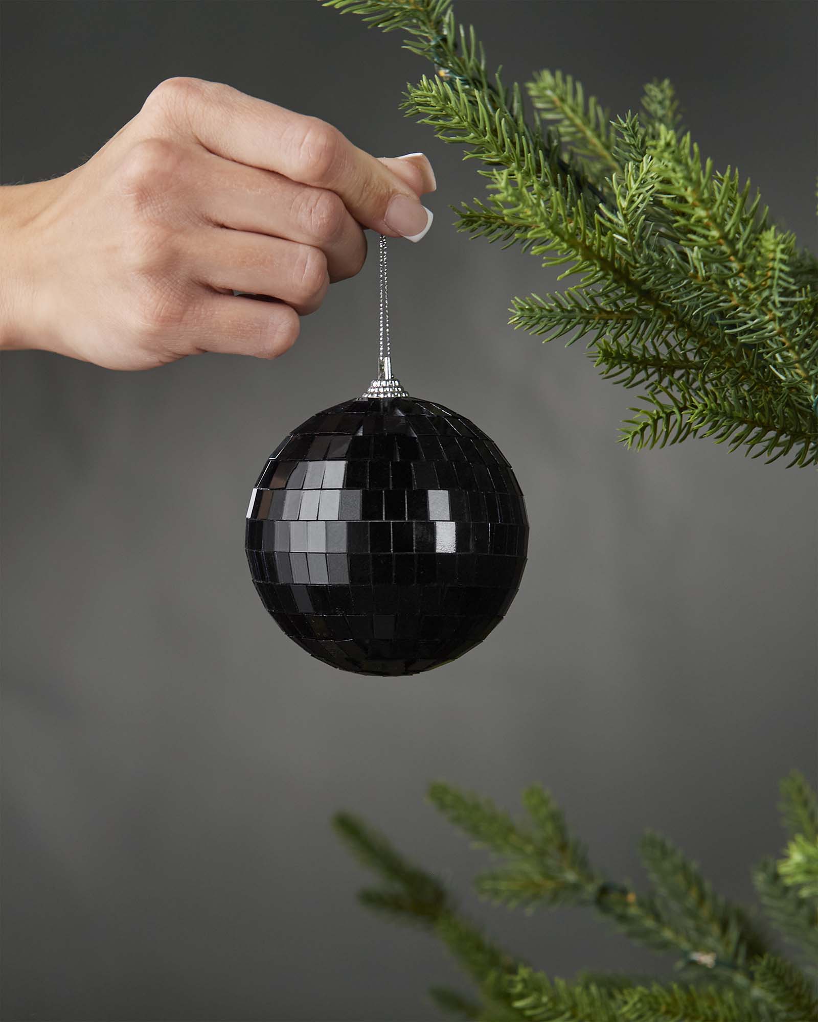 Hand holding a black 8cm disco ball bauble beside a Christmas tree.
