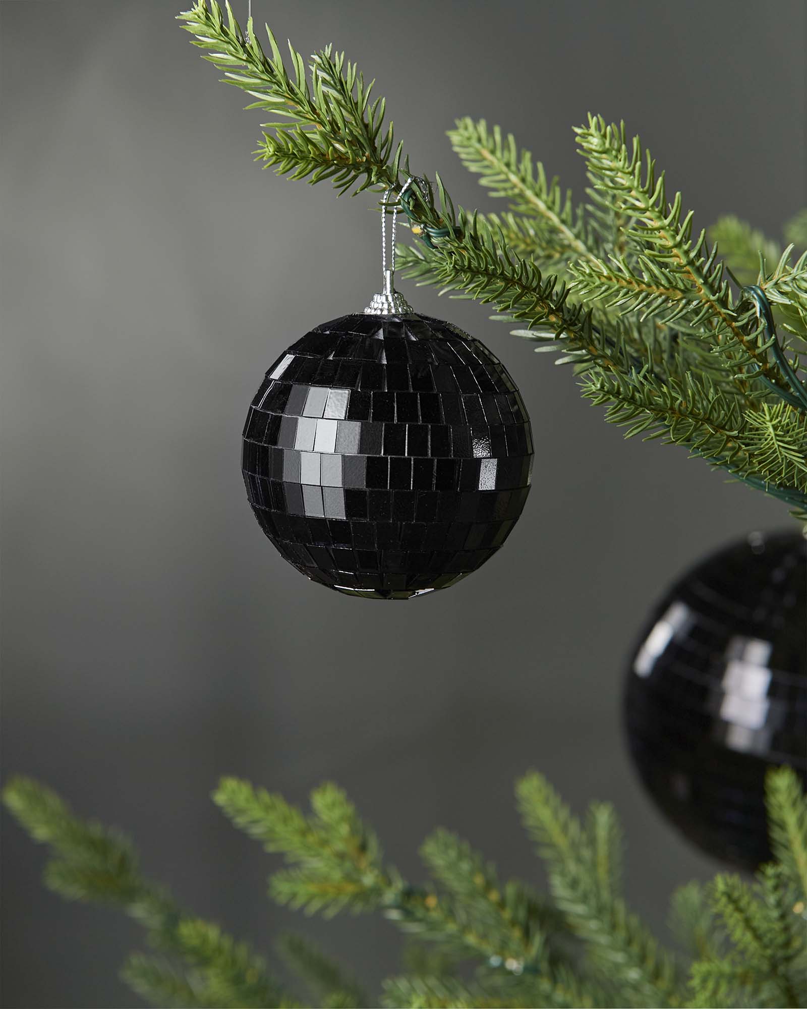 Black 8cm disco ball bauble hanging on a Christmas tree branch.
