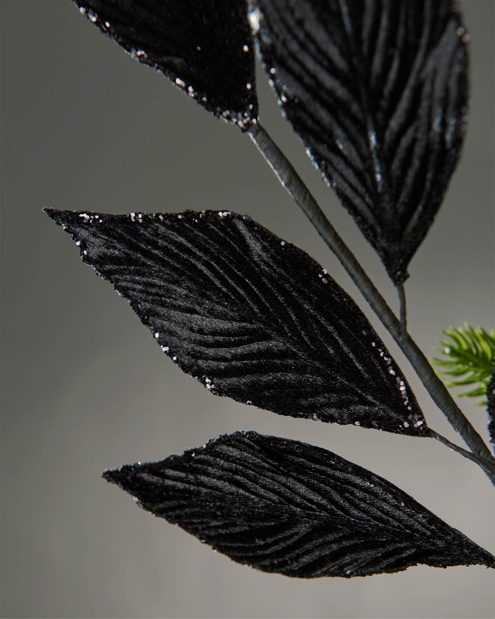 Close-up of a 72 cm black artificial leaf spray showing textured leaves with glitter edging on a black stem.