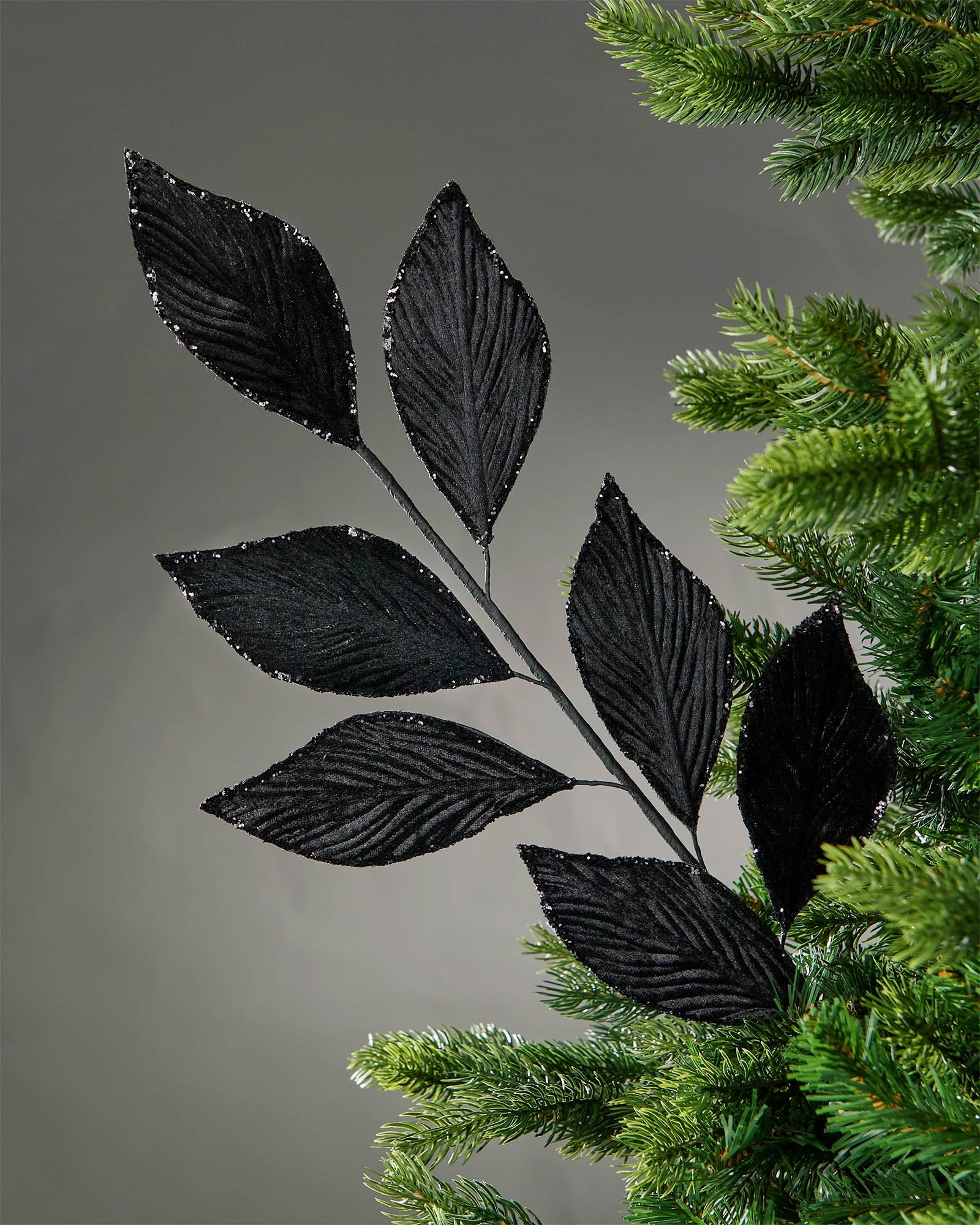 72 cm black artificial leaf spray displayed in a Christmas tree, with elongated leaves and glitter-trimmed edges.