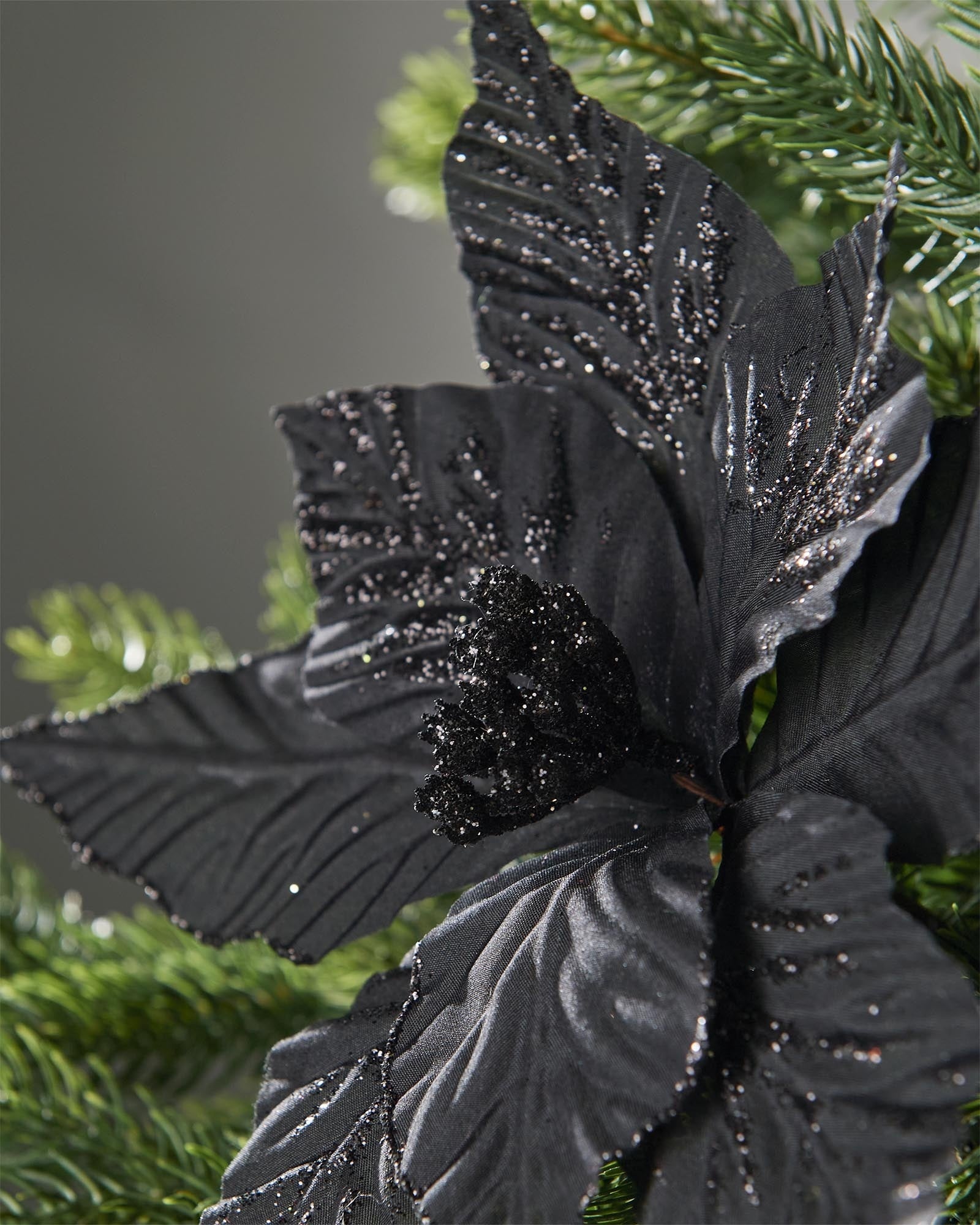 Close-up of a 25 cm black artificial poinsettia flower showing textured petals and a glittered centre.
