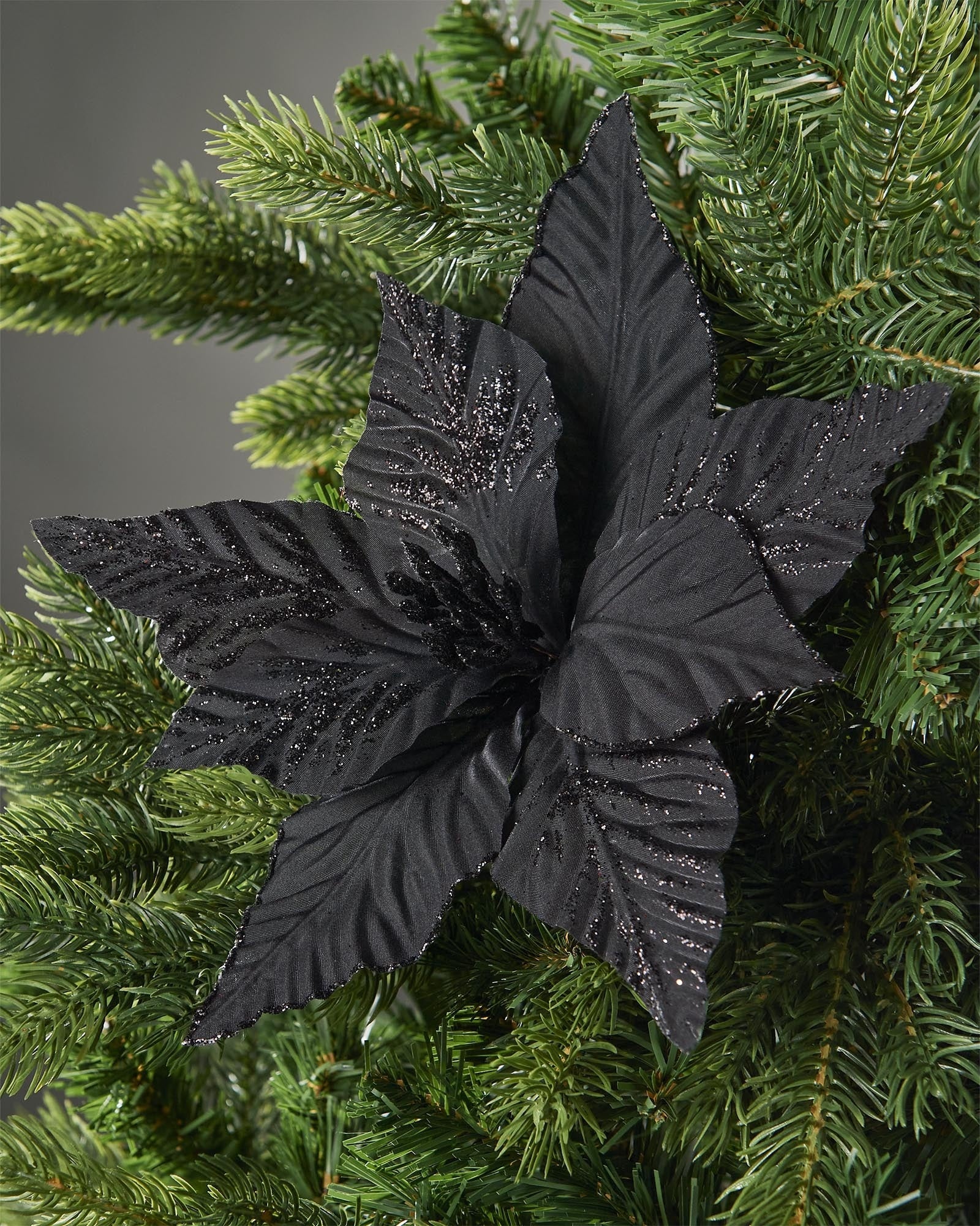 25 cm black artificial poinsettia flower displayed in a Christmas tree, with layered fabric petals and subtle glitter detail.