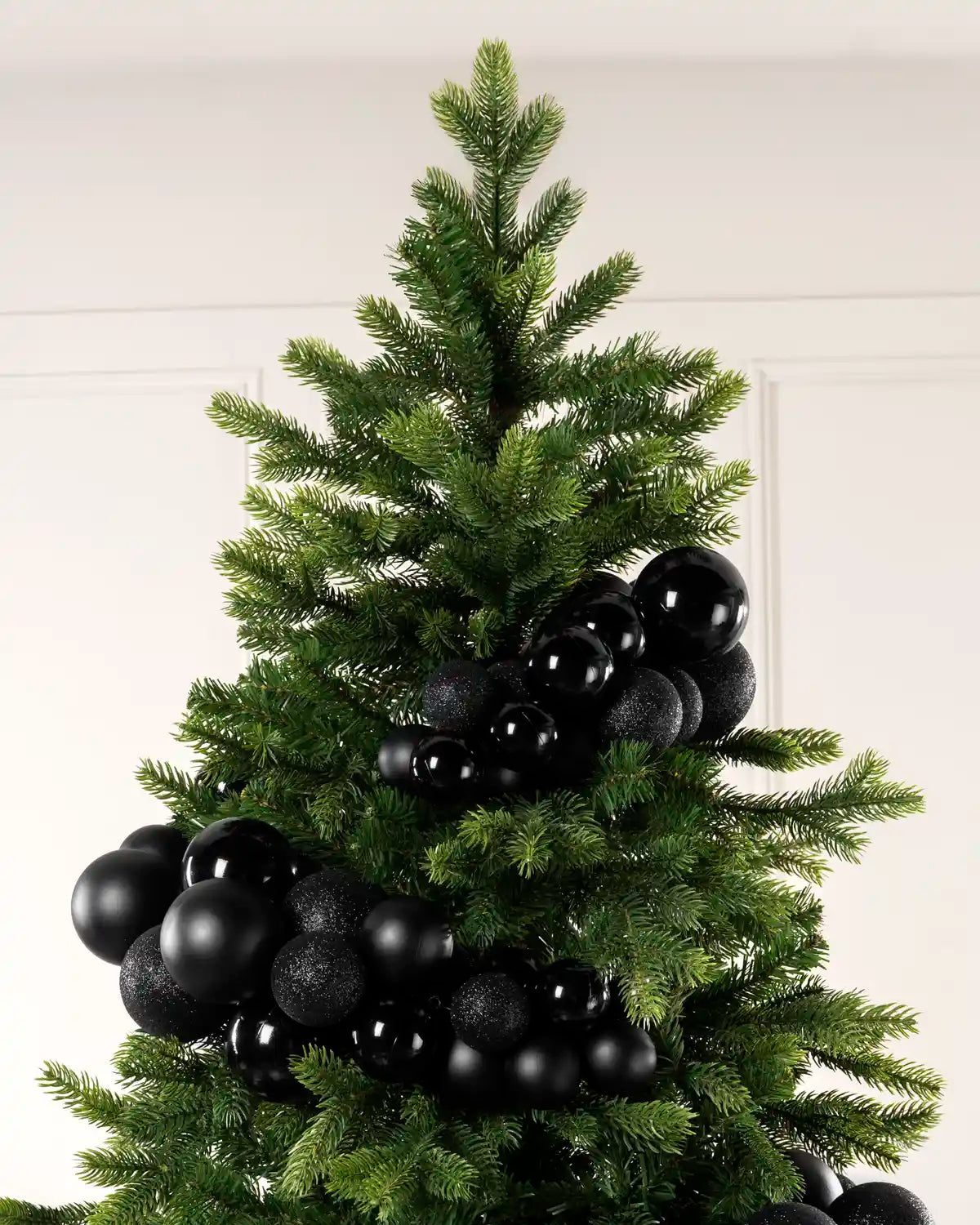 Black bauble cluster arch arranged through the upper branches of a green Christmas tree.