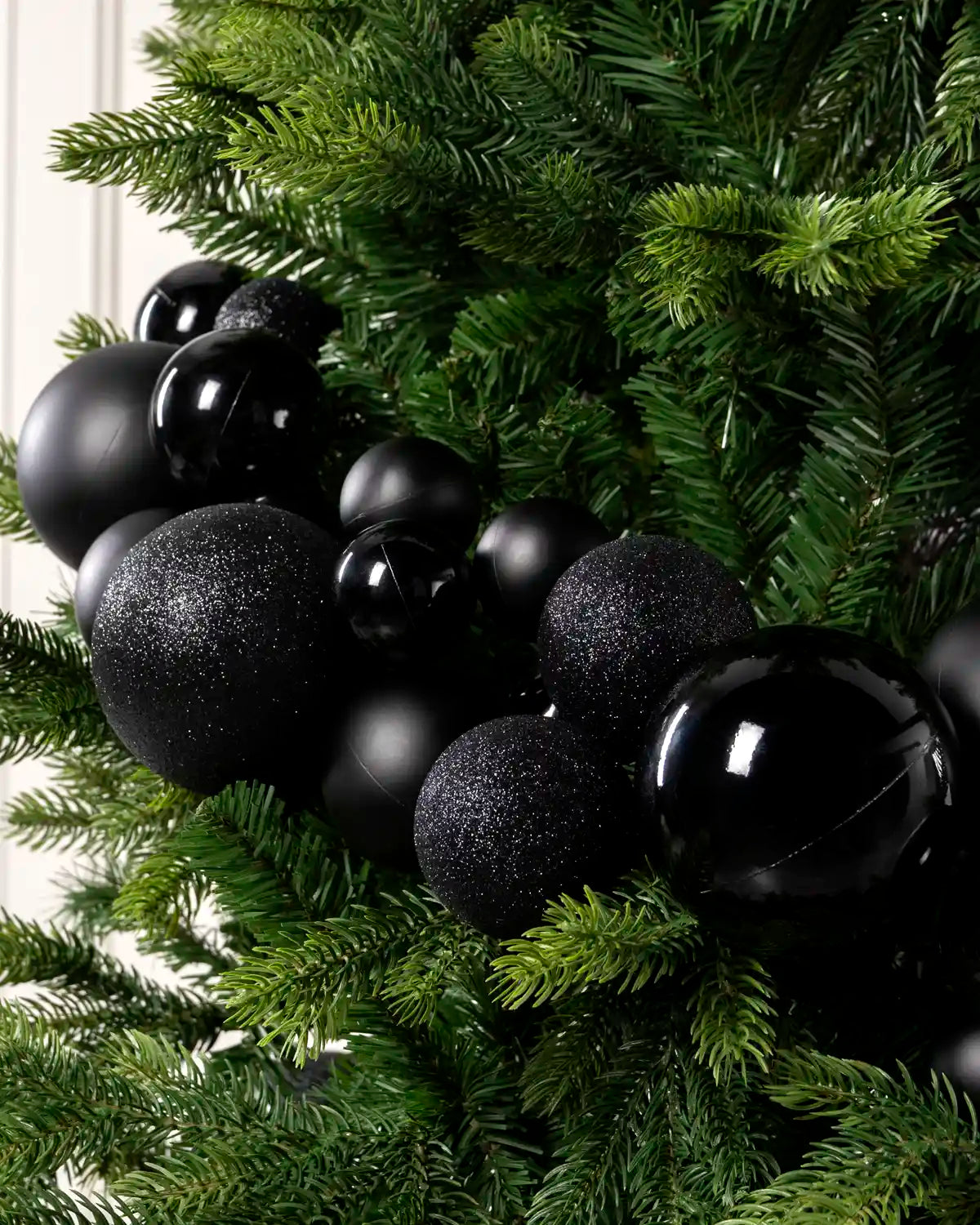 Close-up of black bauble garland on a Christmas tree showing mixed sizes, matt, shiny and glitter finishes.