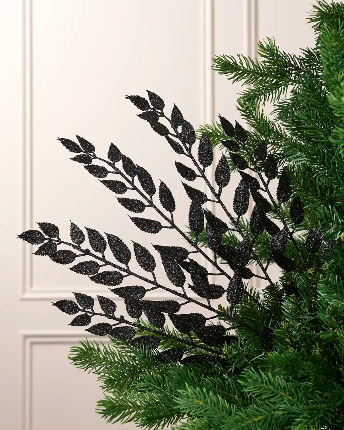 Black leaf Christmas tree spray arranged between green Christmas tree branches.