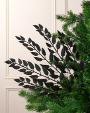 Black leaf Christmas tree spray arranged between green Christmas tree branches.
