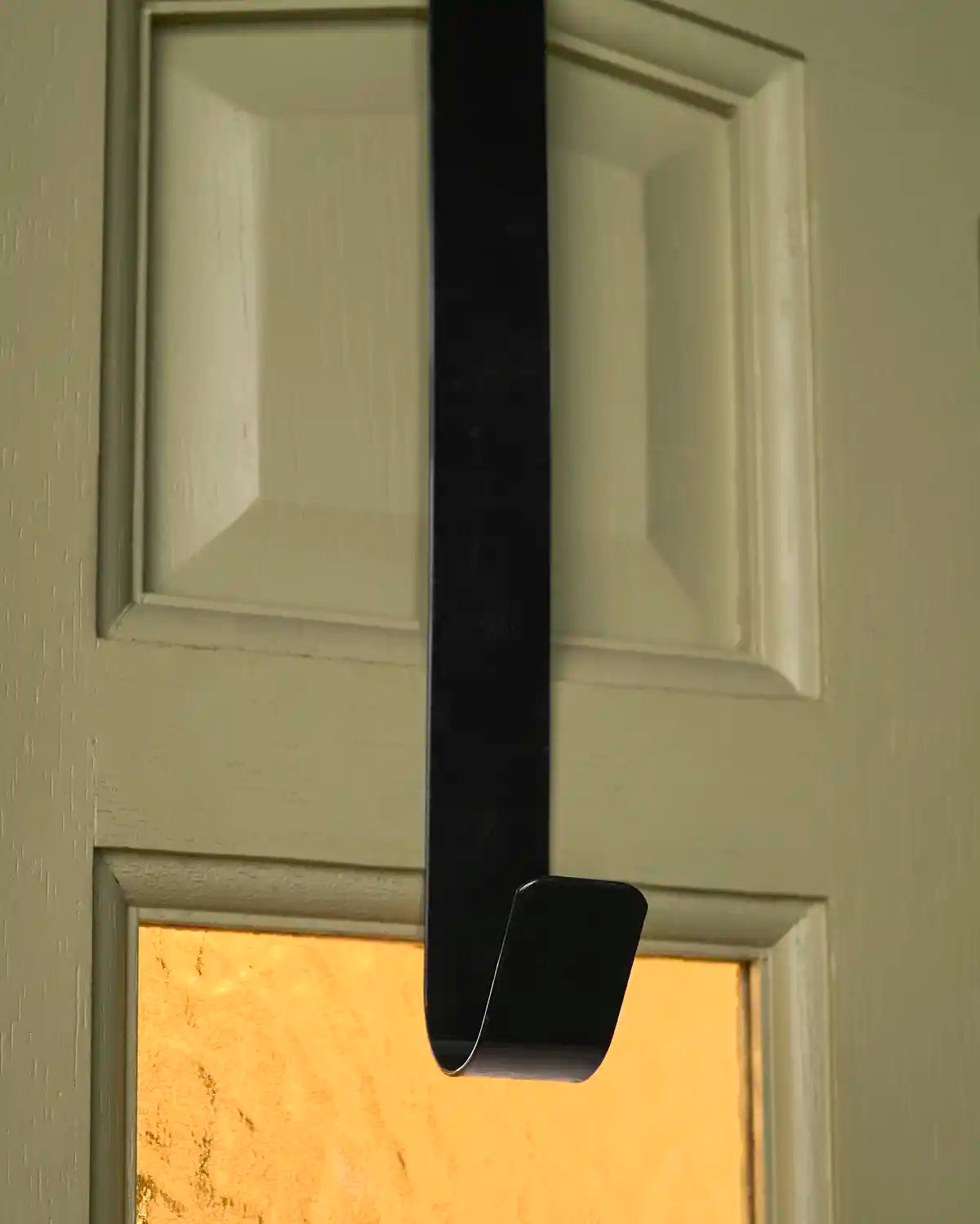 Close-up of the black metal wreath hanger showing the curved lower hook fitted on a door.