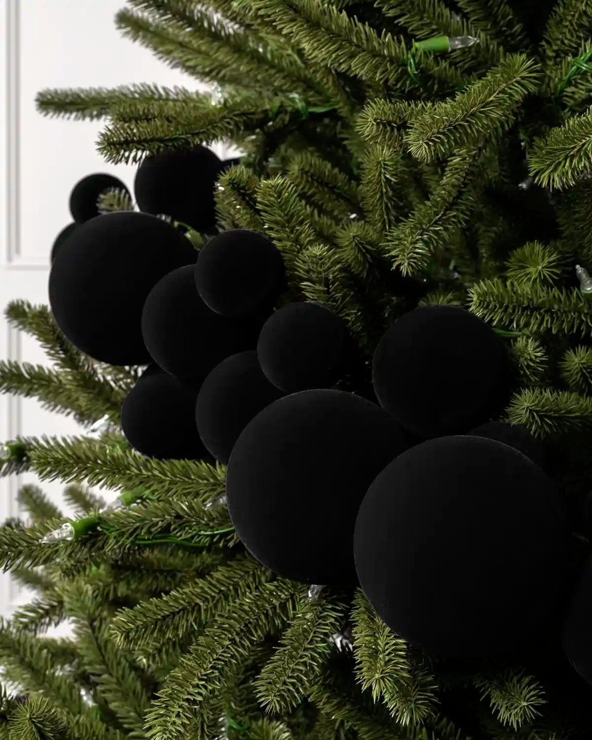 Close-up of black velvet bauble garland on a Christmas tree showing the soft textured finish and mixed bauble sizes.