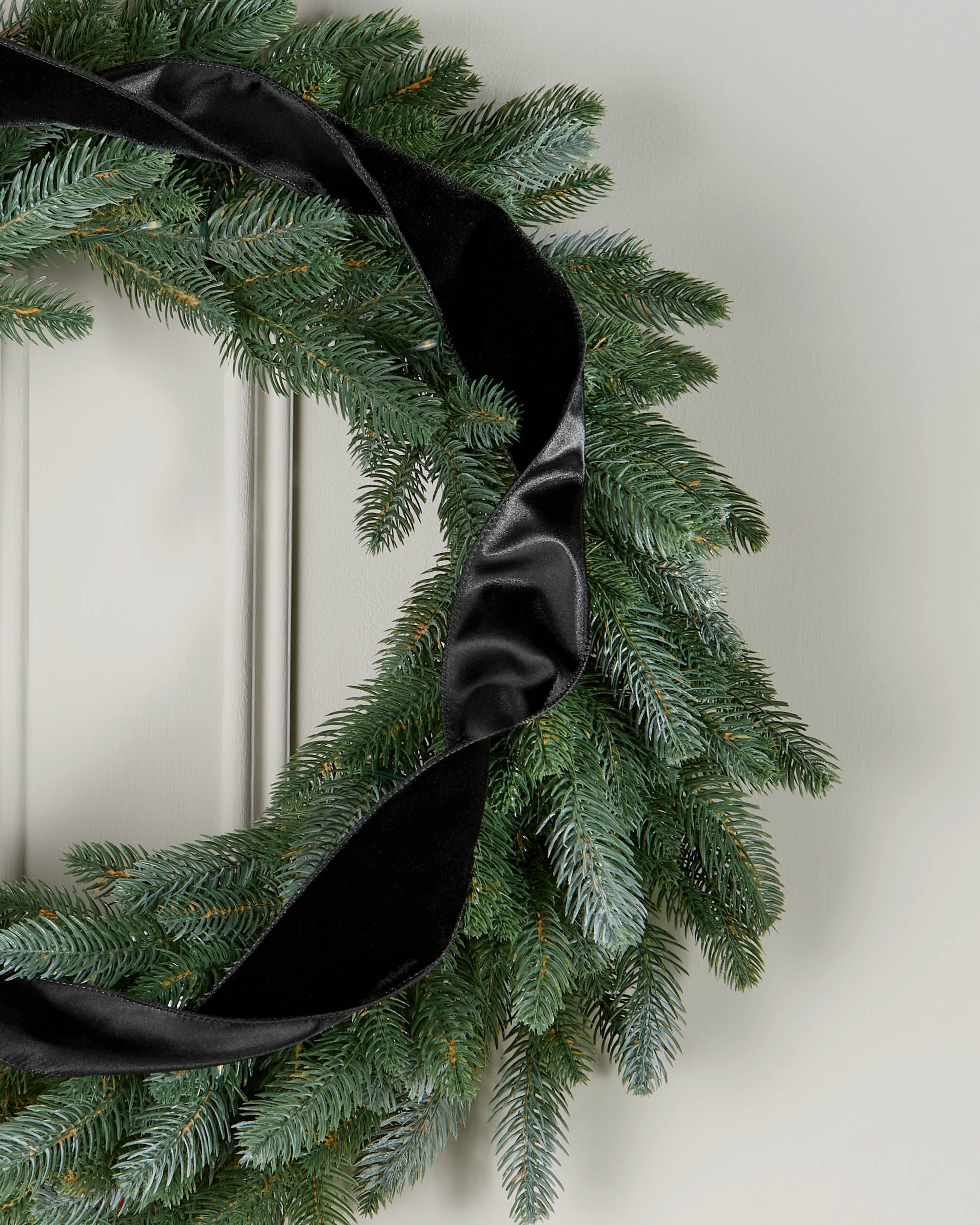 Black velvet ribbon styled in a loose spiral on a green Christmas wreath.